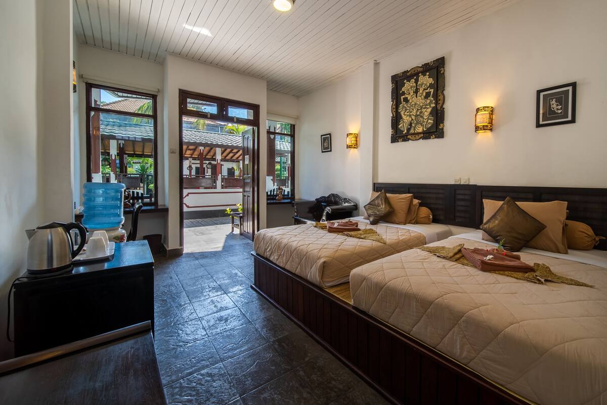 A hotel room with two beds, a coffee maker, a water dispenser, and a view of the outside.