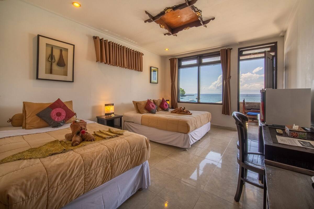 A hotel room with two beds, a desk, and a view of the sea.