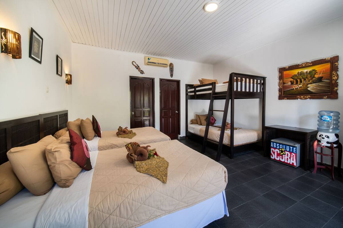 A hotel room with two bunk beds, a bed with a quilted cover, and a water dispenser.