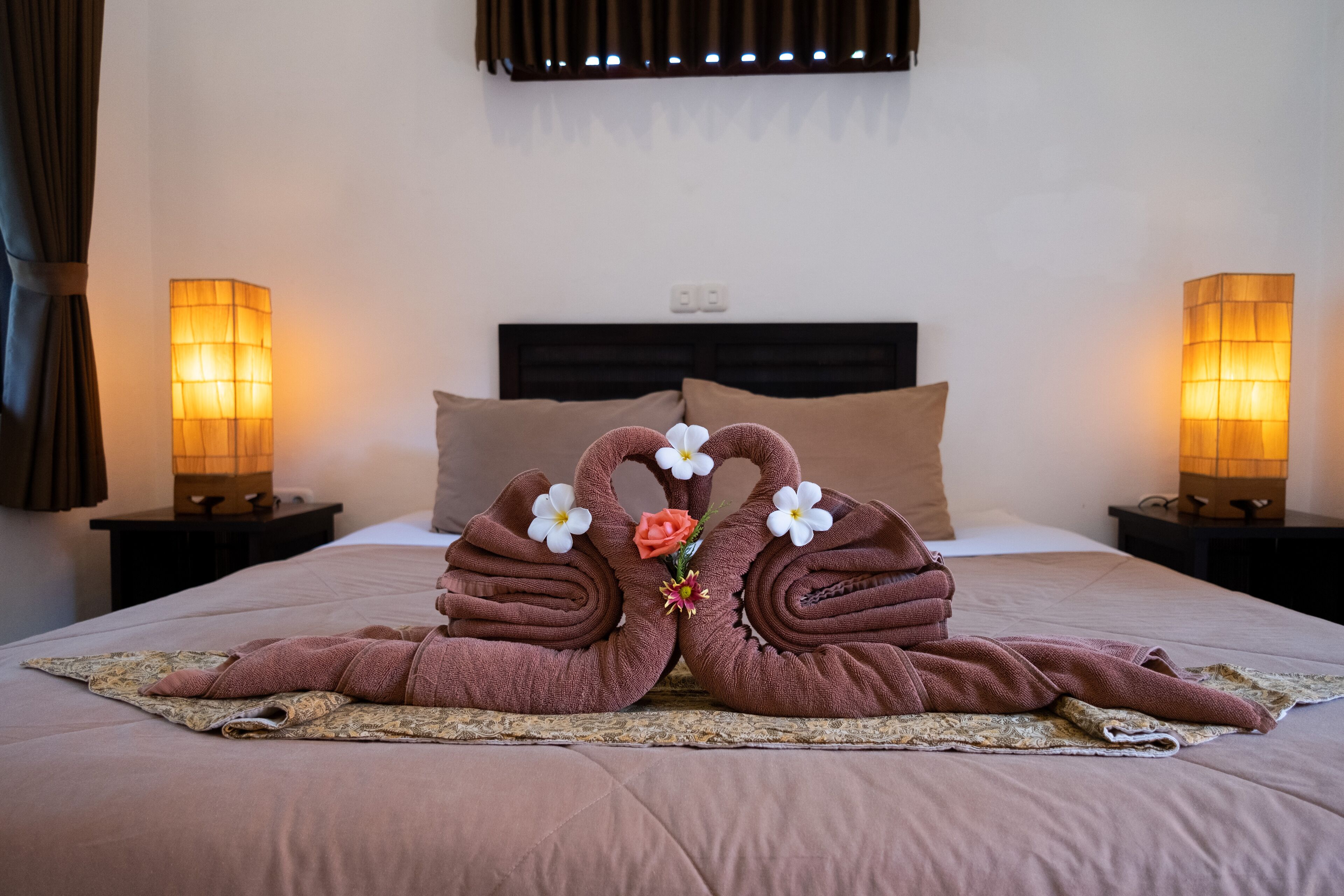 A neatly made bed with a brown blanket, two pillows, and a decorative towel arrangement in the center.