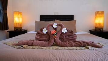 A neatly made bed with a brown blanket, two pillows, and a decorative towel arrangement in the center.