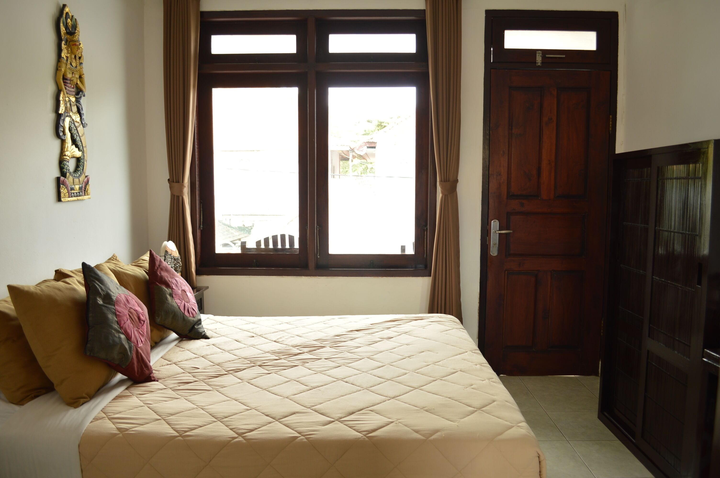 A bedroom with a bed, curtains, a wooden door, and a wall decoration.