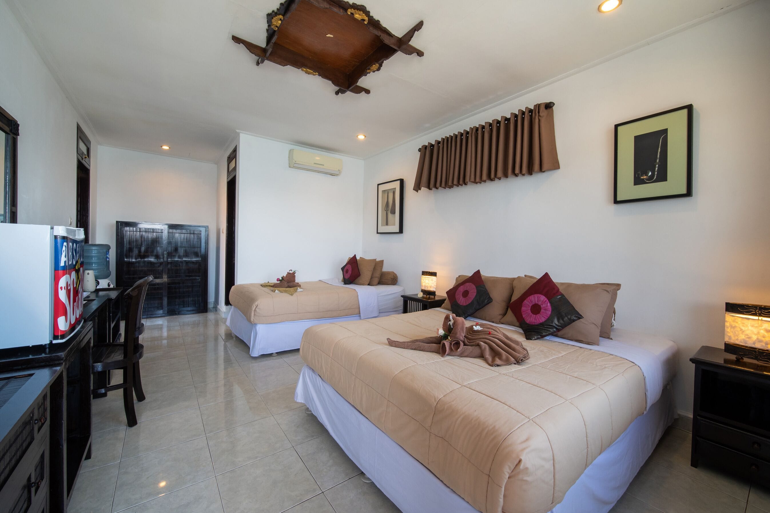 A hotel room with two beds, a desk, a chair, a TV, and a ceiling fan.