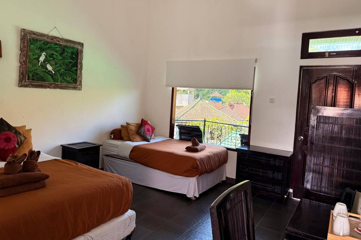 A hotel room with two beds, a TV, a balcony with a view of buildings, and a framed picture on the wall.