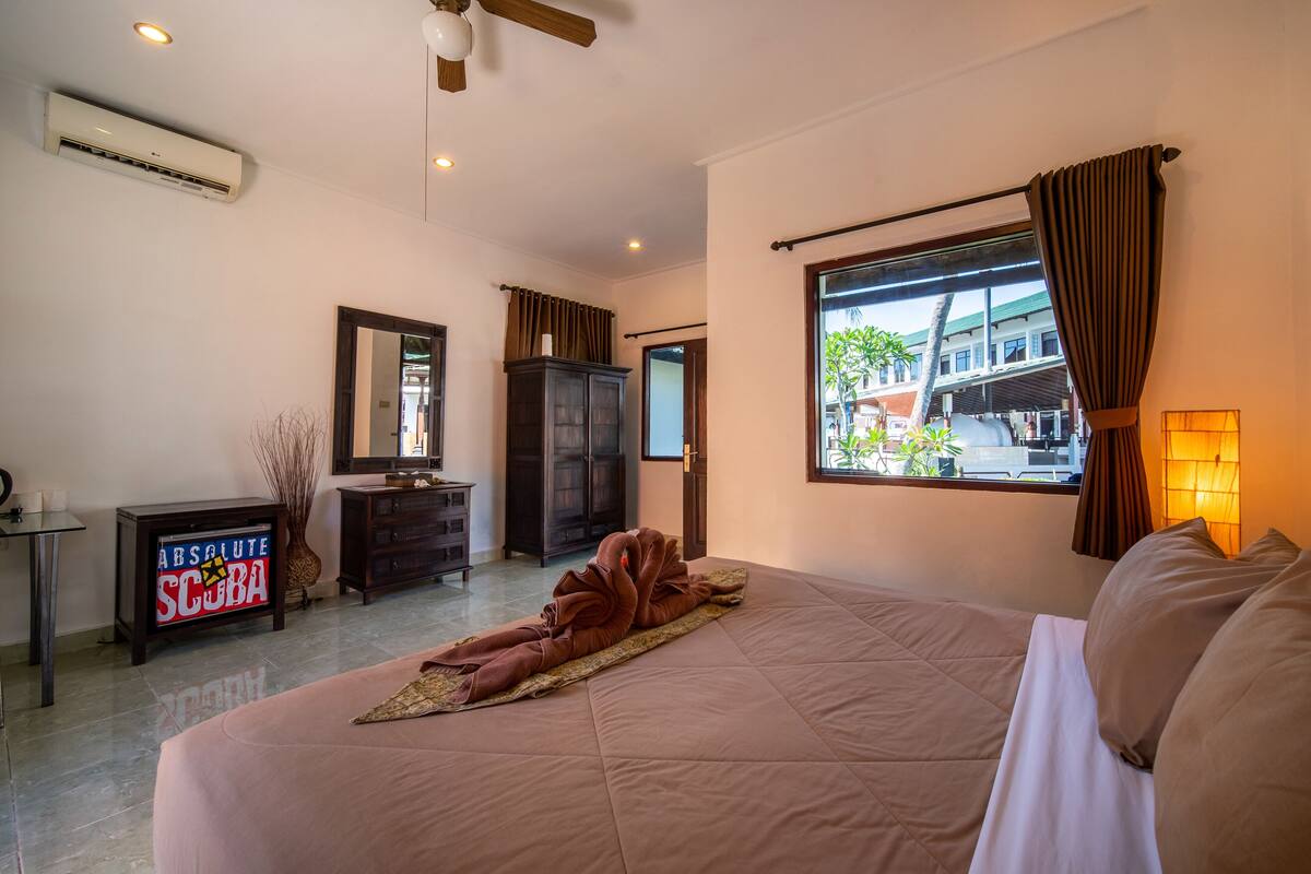 A hotel room with a large bed, a wardrobe, a vanity with a mirror, and a window with curtains.
