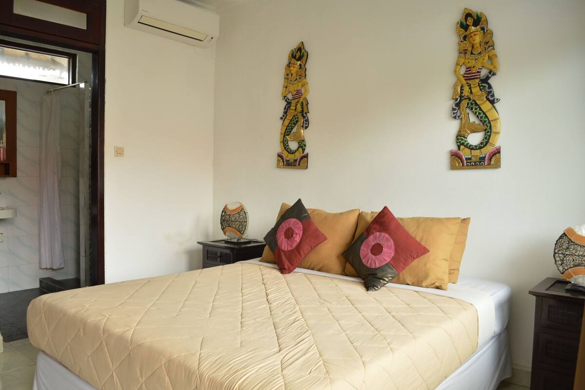 A hotel room with a large bed, two wall-mounted decorative pieces, and a window with a curtain.