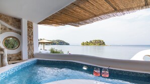 Un jacuzzi con vista al mar, una copa de bebida rosada y conchas marinas en el borde.