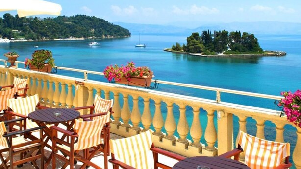 Terraza con mesas al aire libre, con vista a un mar tranquilo con barcos y una isla.