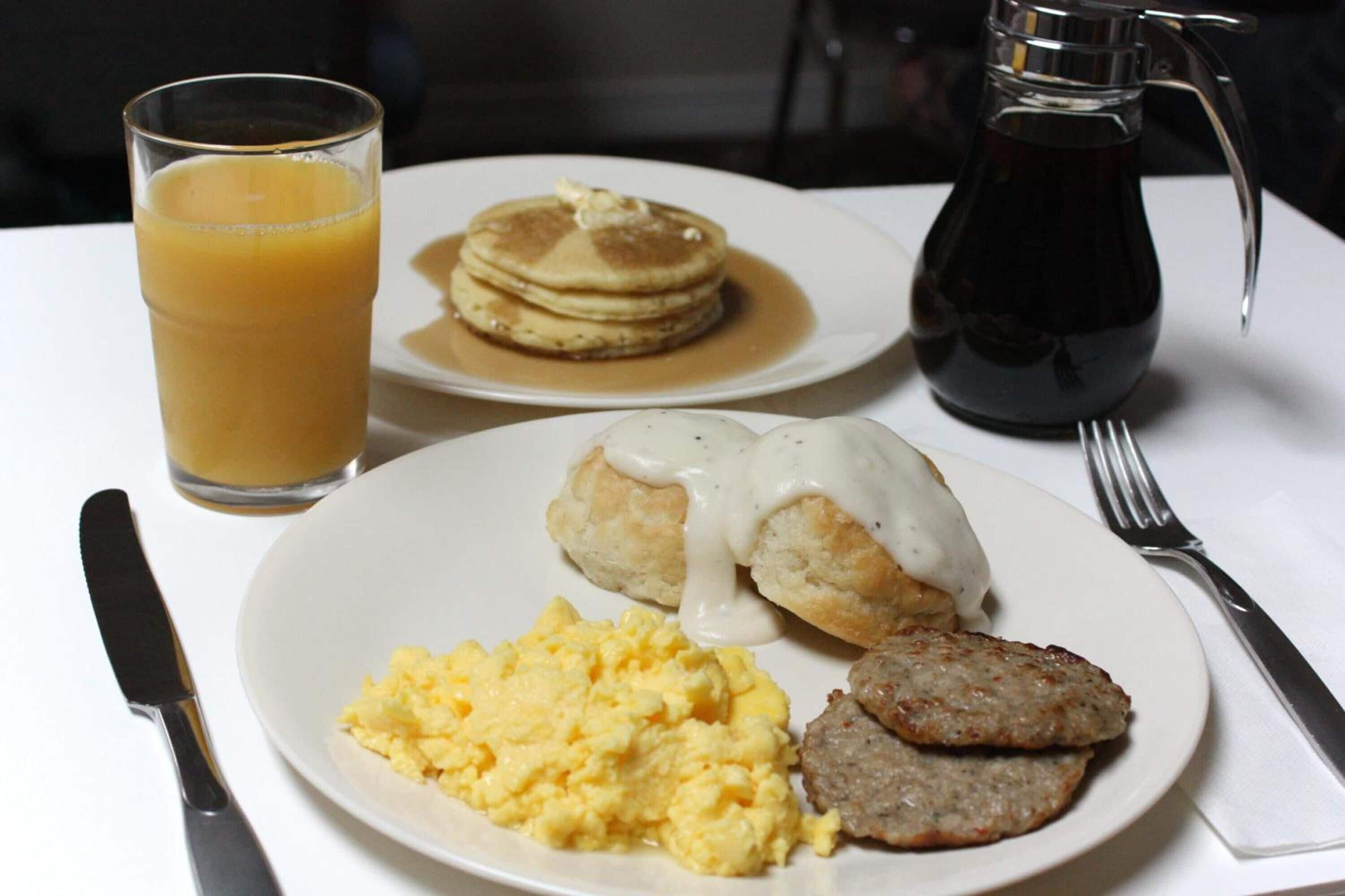 A breakfast plate with pancakes, eggs, sausage, and a glass of orange juice.