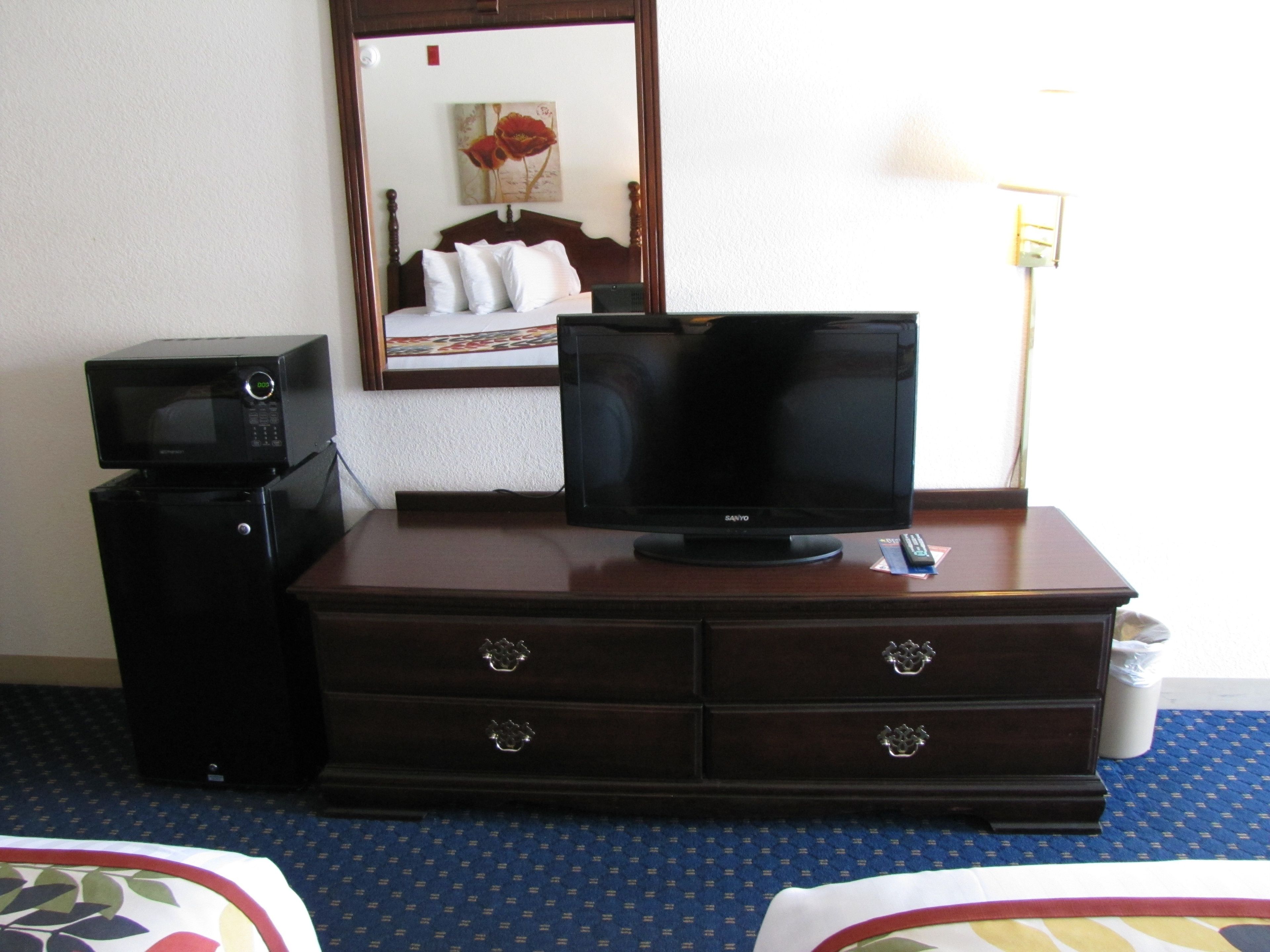Une chambre d’hôtel avec une télévision posée sur une commode en bois, un four à micro-ondes et un lit recouvert d’une couvre-lit à motifs.