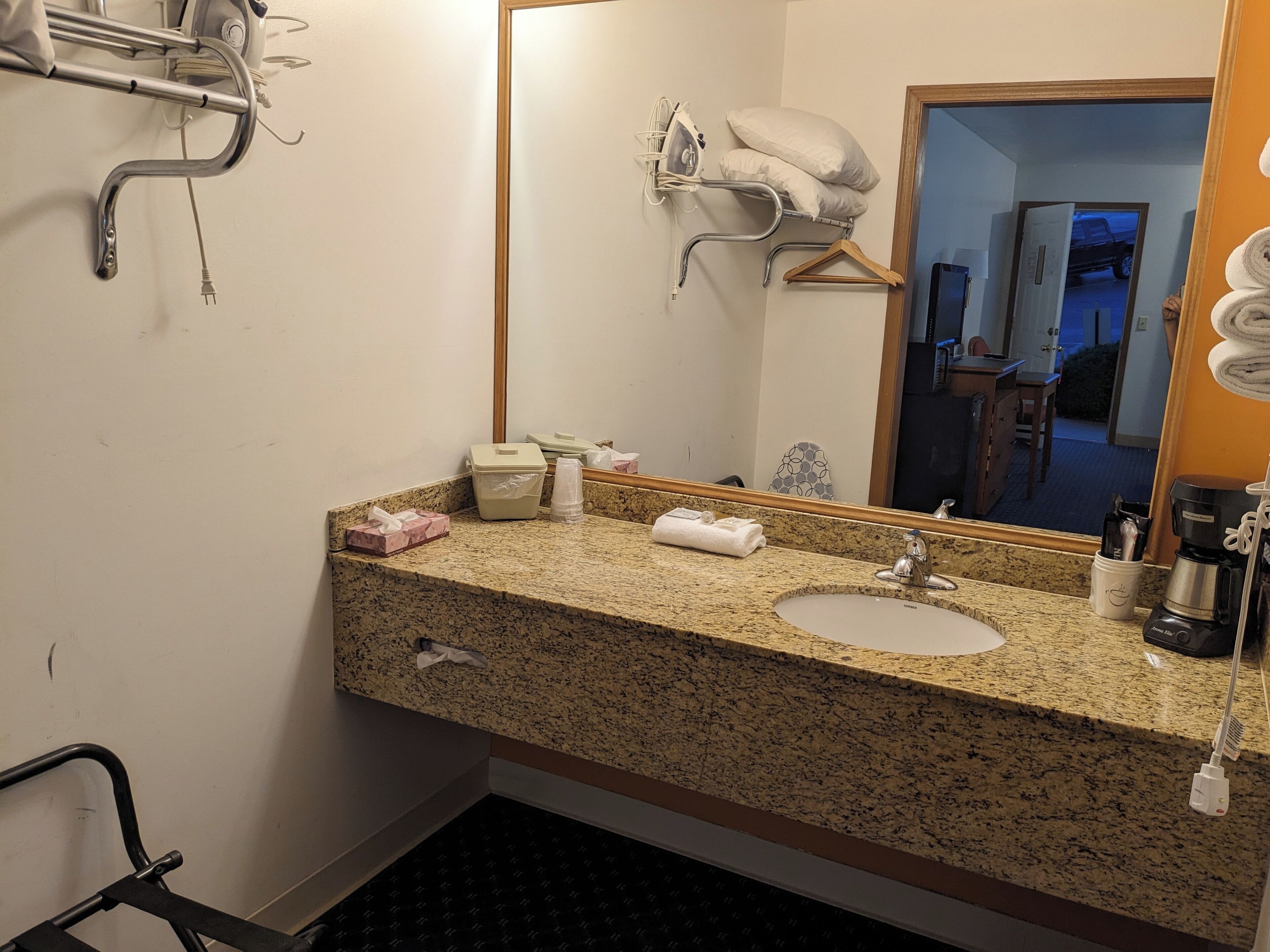 A hotel bathroom with a granite countertop, a sink, a mirror, a towel rack, and a shower area.
