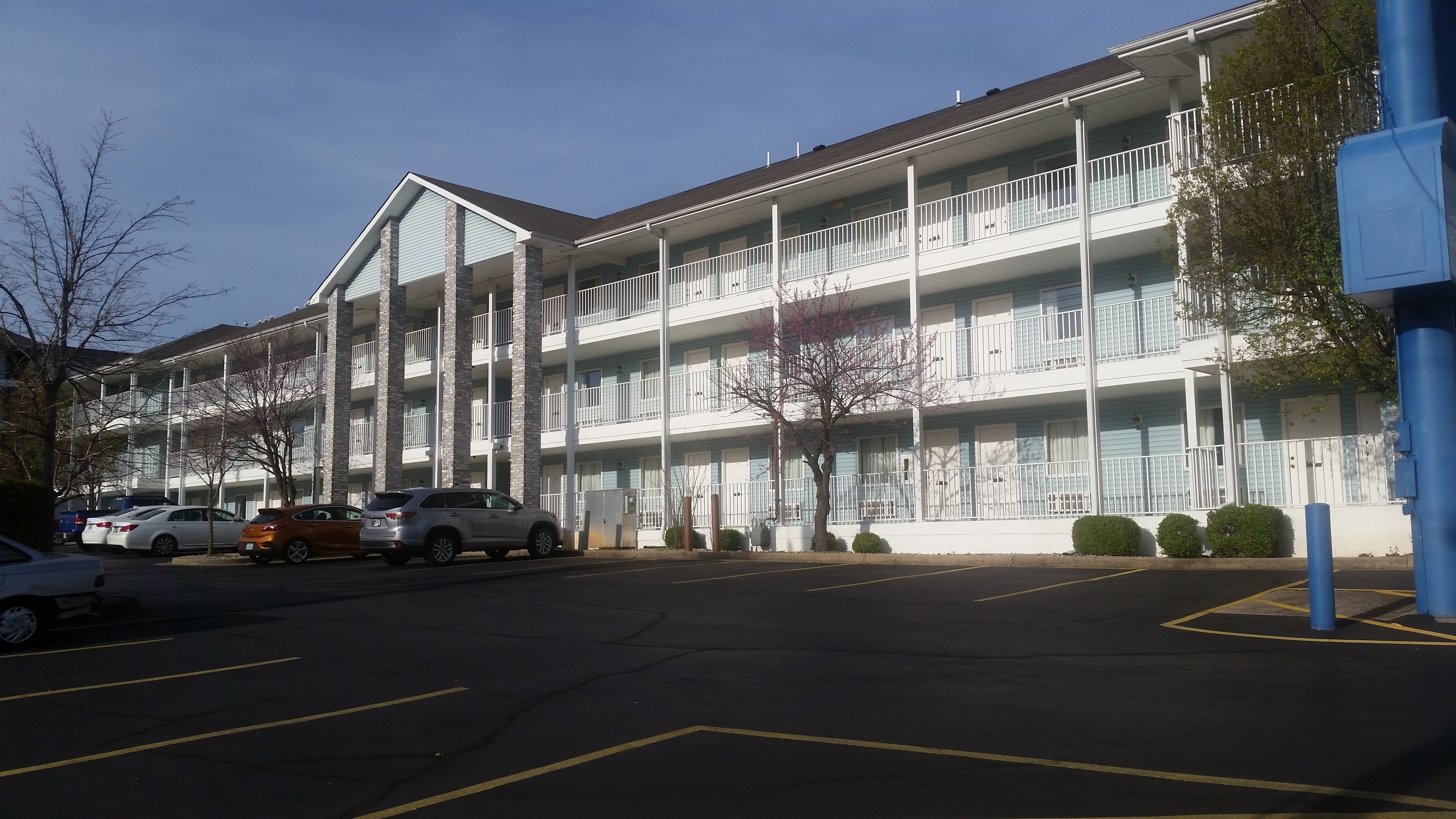 A multi-story hotel with a central atrium, parking lot, and a row of parked cars.