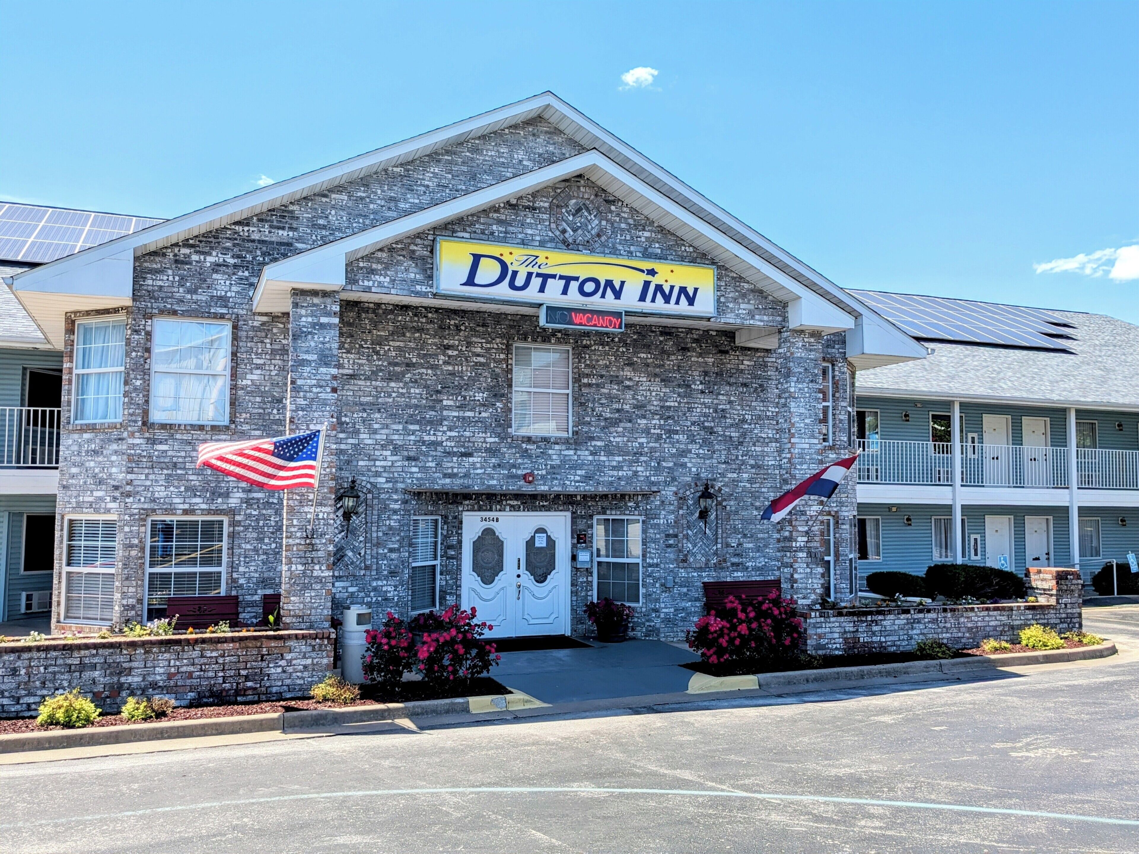 A Dutton Inn building with a stone facade, a signboard, and two American flags.