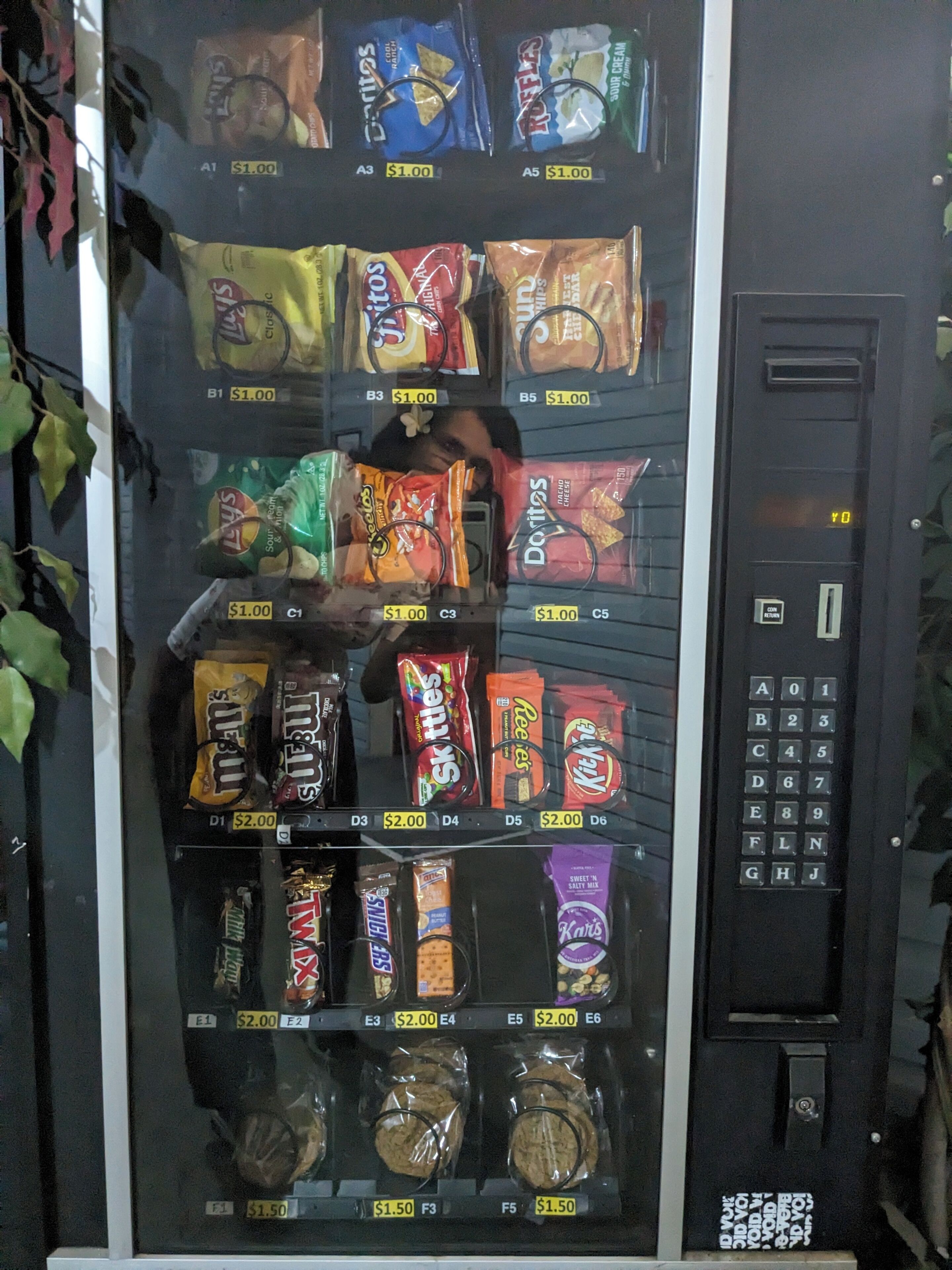 A vending machine stocked with snacks and cookies, including brands like Doritos and Reese's.