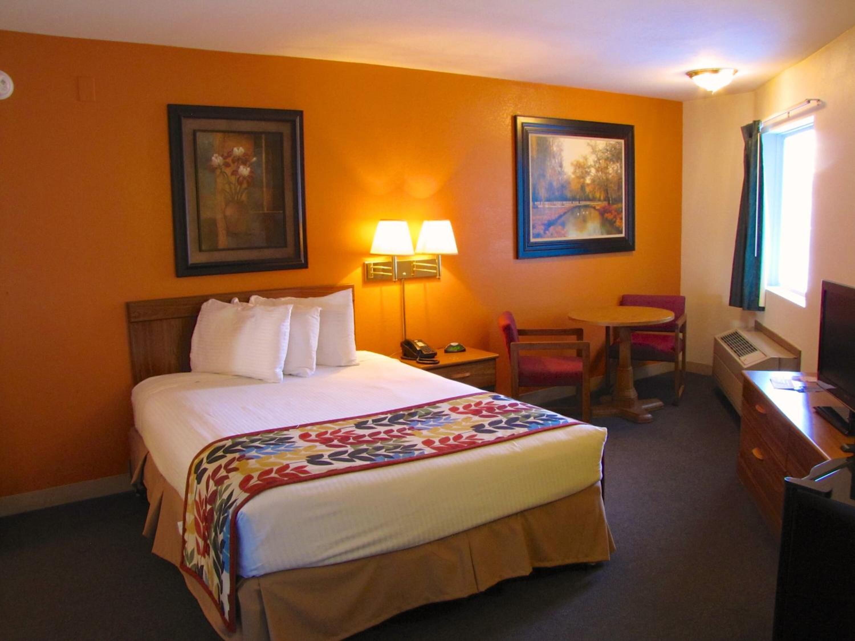 A hotel room with a bed, a desk, a chair, two lamps, and two framed pictures on the wall.
