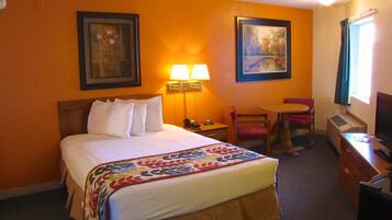 A hotel room with a bed, a desk, a chair, two lamps, and two framed pictures on the wall.