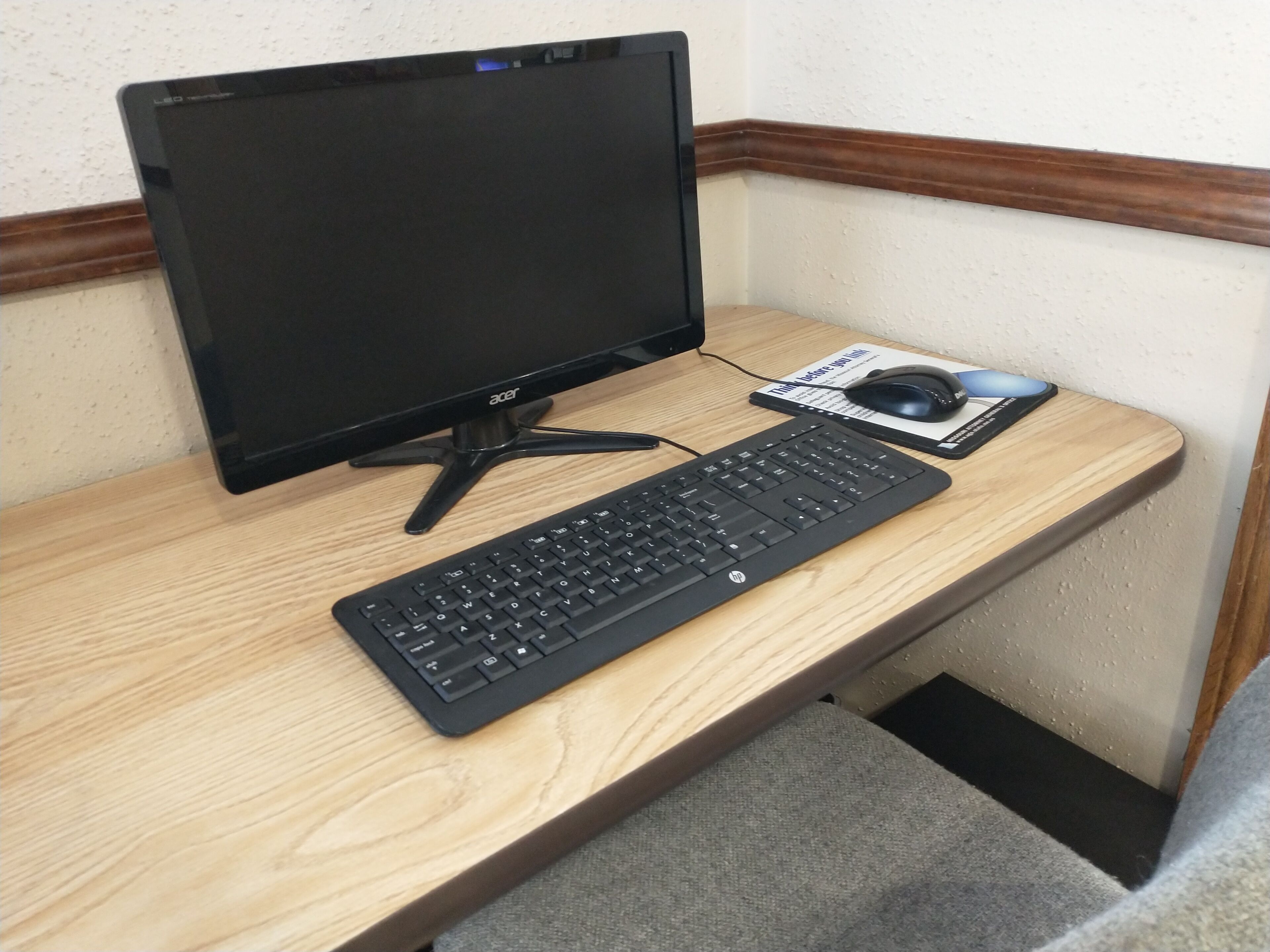 A corner desk with a black monitor, black keyboard, and a mouse on a wooden desk.