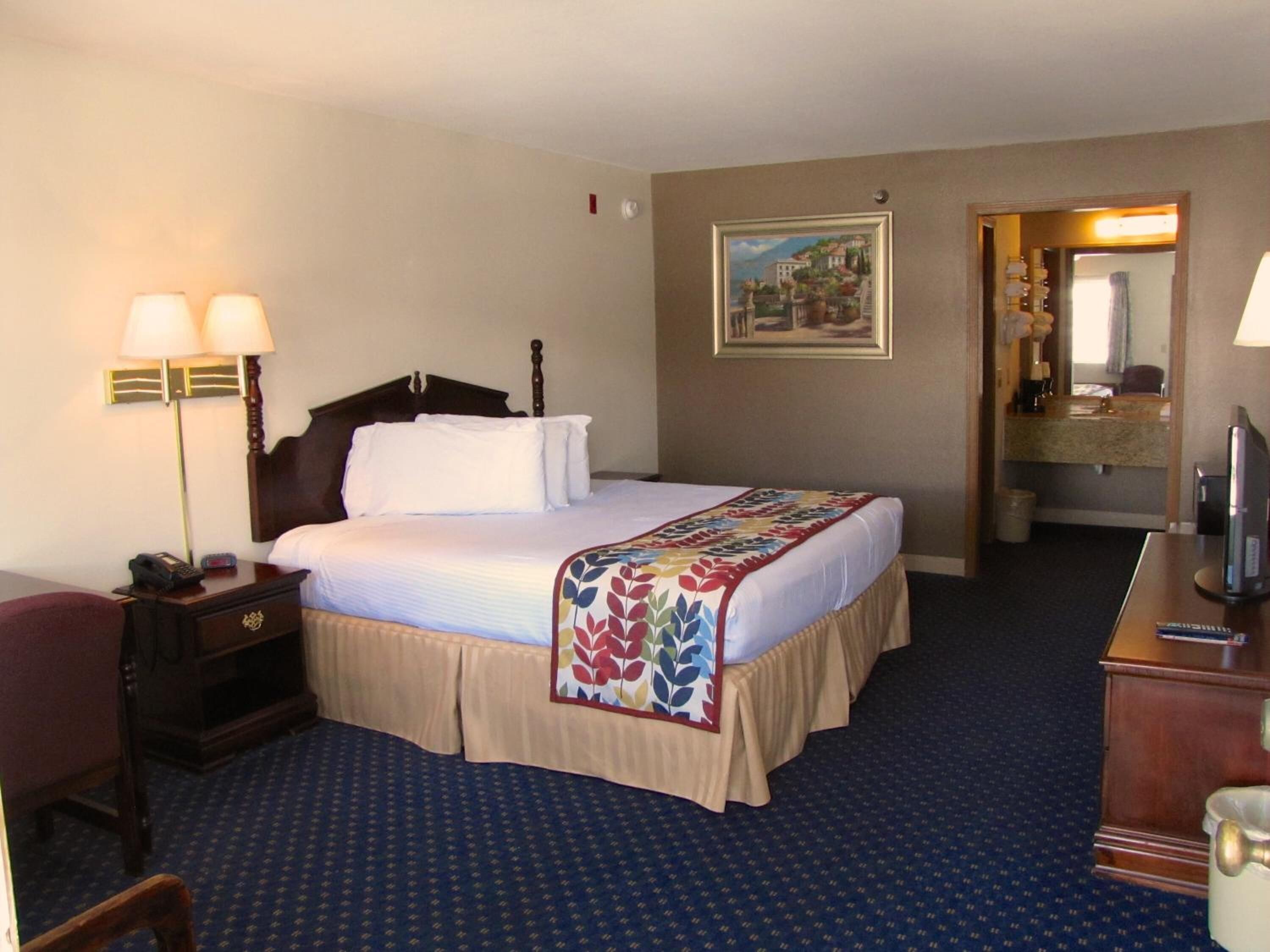 A hotel room with a bed, bedside lamps, a desk with a telephone, a television, and a bathroom visible through an open door.