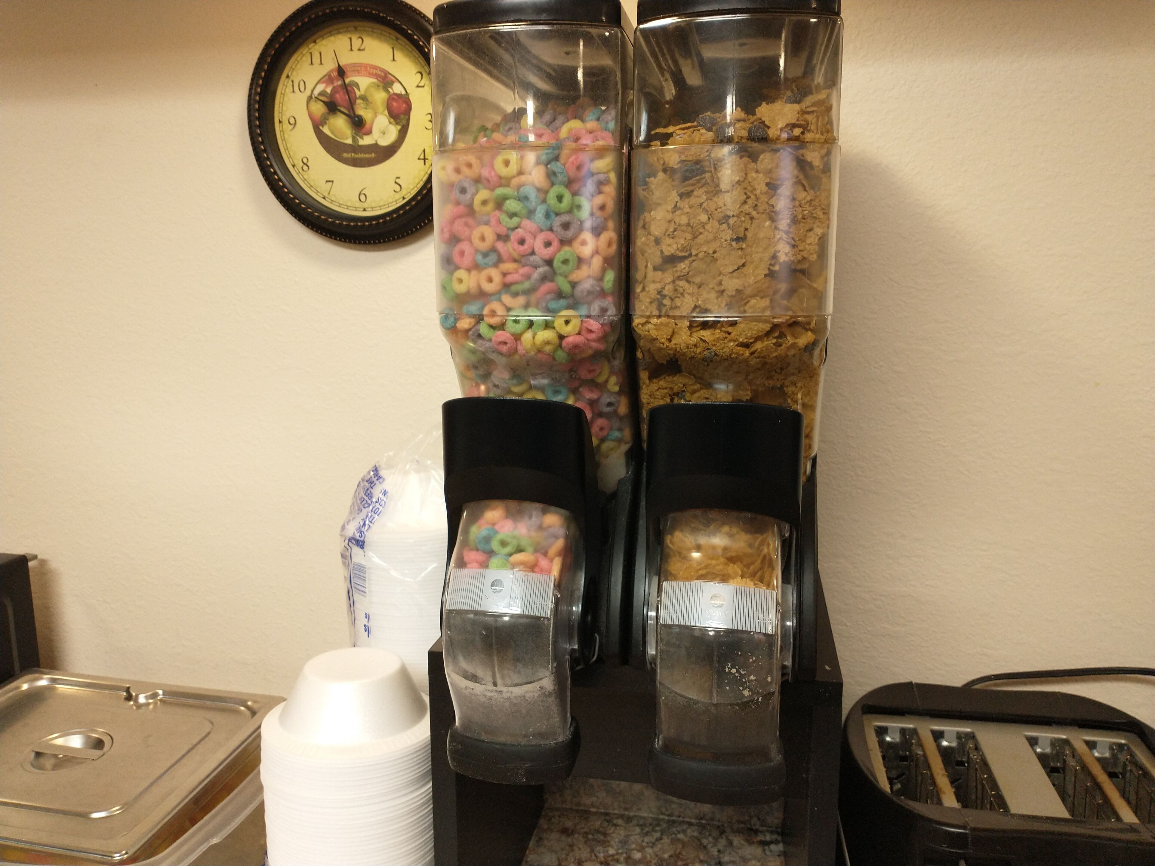 Un dispensador de aperitivos con cereales y leche de cereales, un reloj y un tostador.