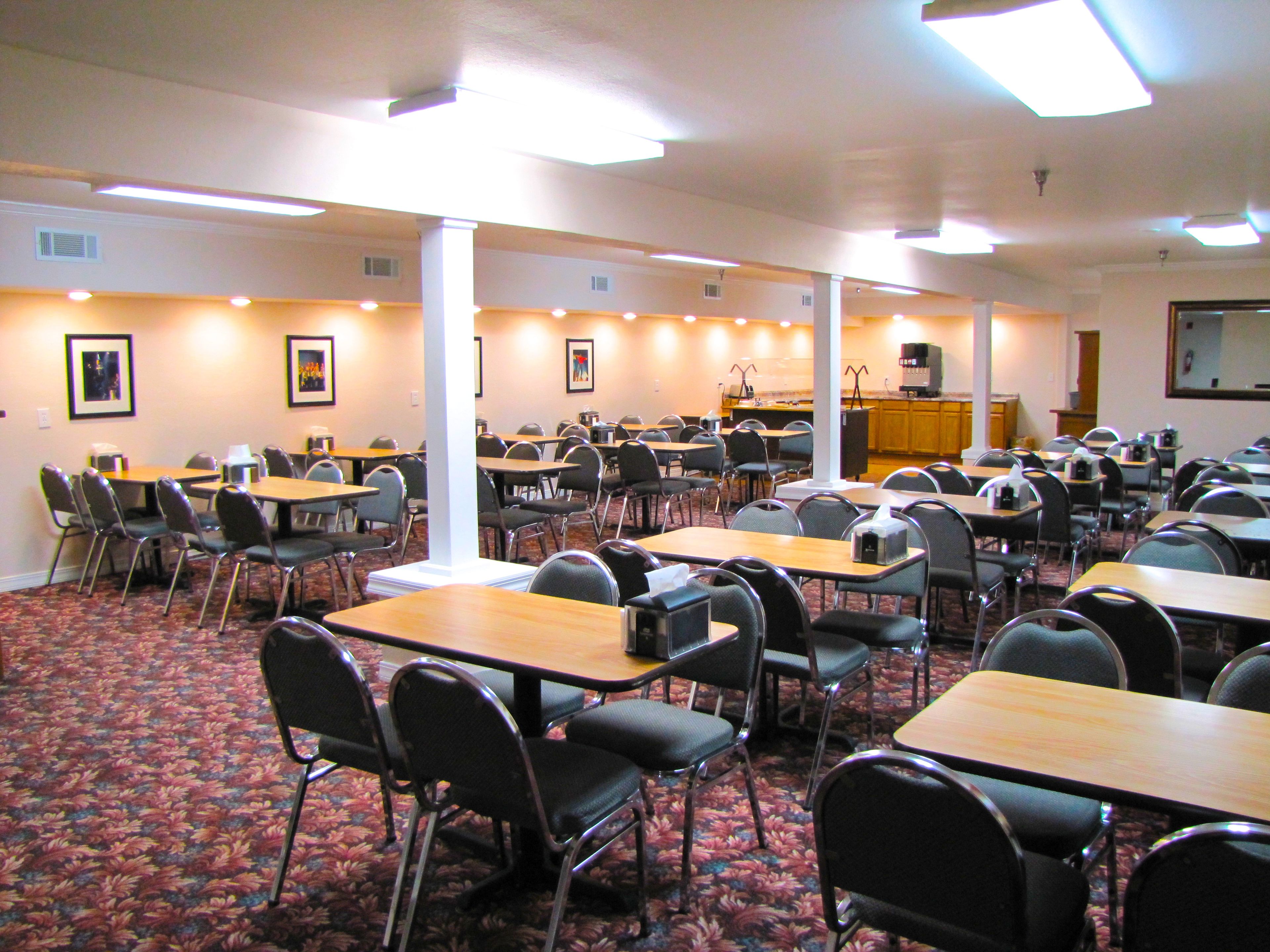 A conference room with multiple tables and chairs, carpeted floor, and ceiling lights.