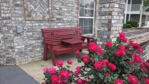 A brick building with a red bench and a rose bush in front.