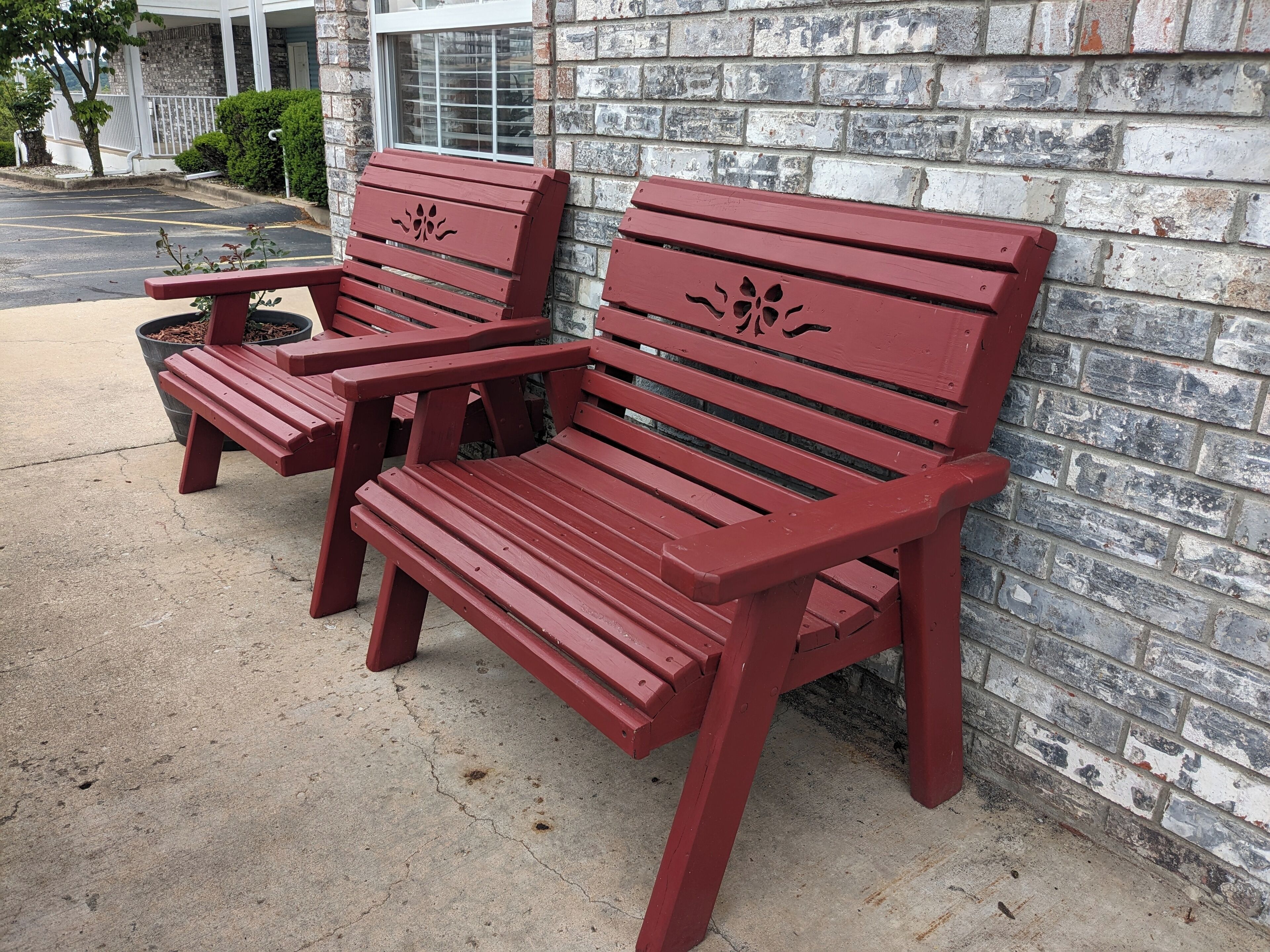 Two red wooden benches with slatted seats and backs, positioned against a brick wall with a window above.