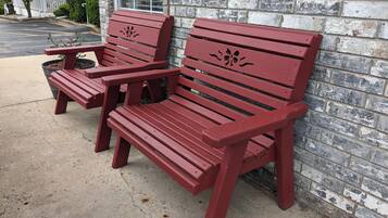 Two red wooden benches with slatted seats and backs, positioned against a brick wall with a window above.