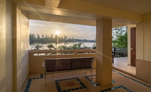 Ein Balkon mit einer Sitzbank, Blick auf ein Gewässer und eine ferne Stadtlandschaft.