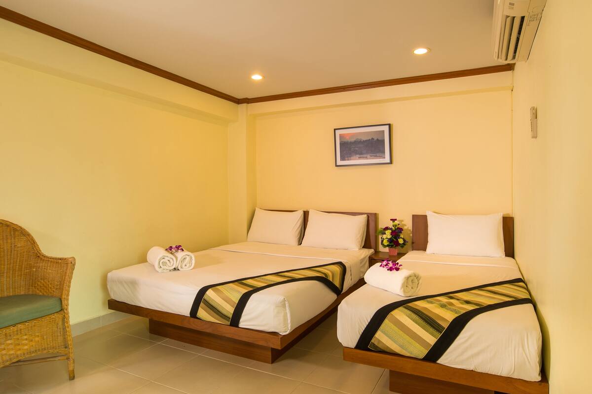 A hotel room with two beds, a wicker chair, and a painting on the wall.