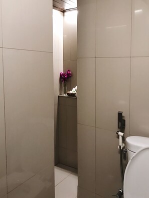 Un baño moderno con ducha, inodoro y un pequeño estante con un florero.