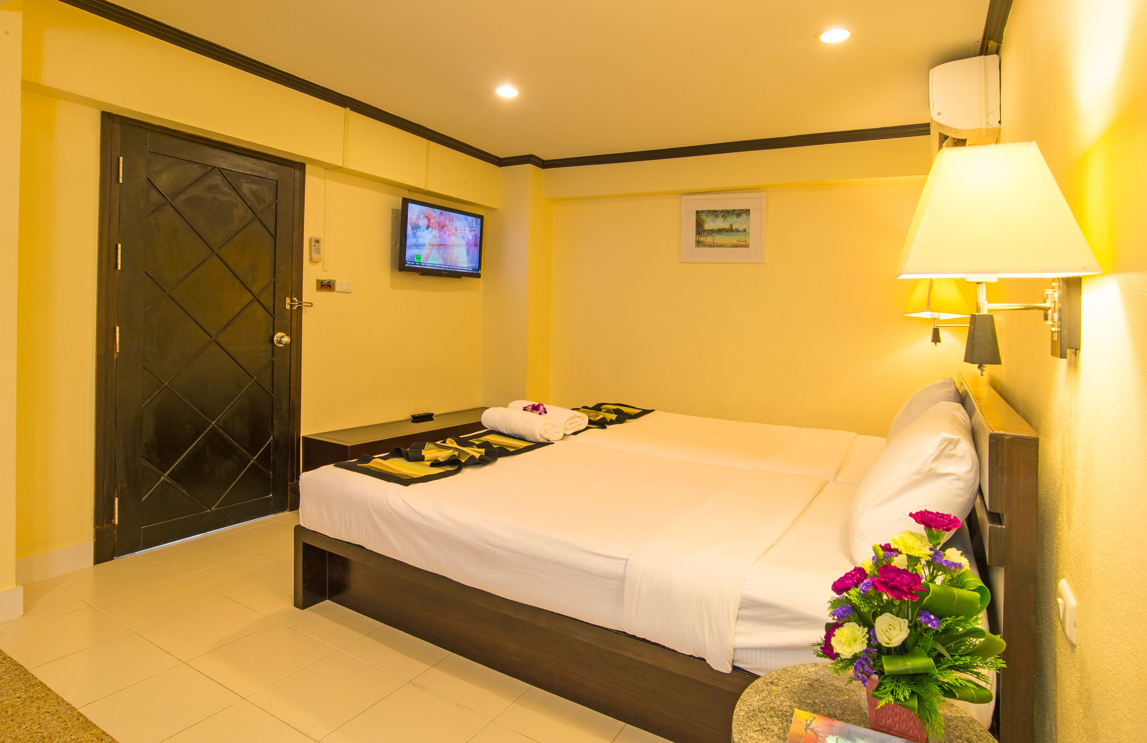 A hotel room with a bed, a TV, a lamp, and a flower arrangement.