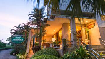 A hotel entrance with a signboard, palm trees, and a well-lit interior.