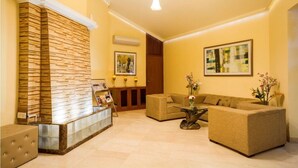 A reception area with a wooden reception desk, a sofa, and a coffee table. There are framed pictures on the walls and a vase with flowers on the coffee table. - 66 Residency - A Boutique Hotel (Jaipur)