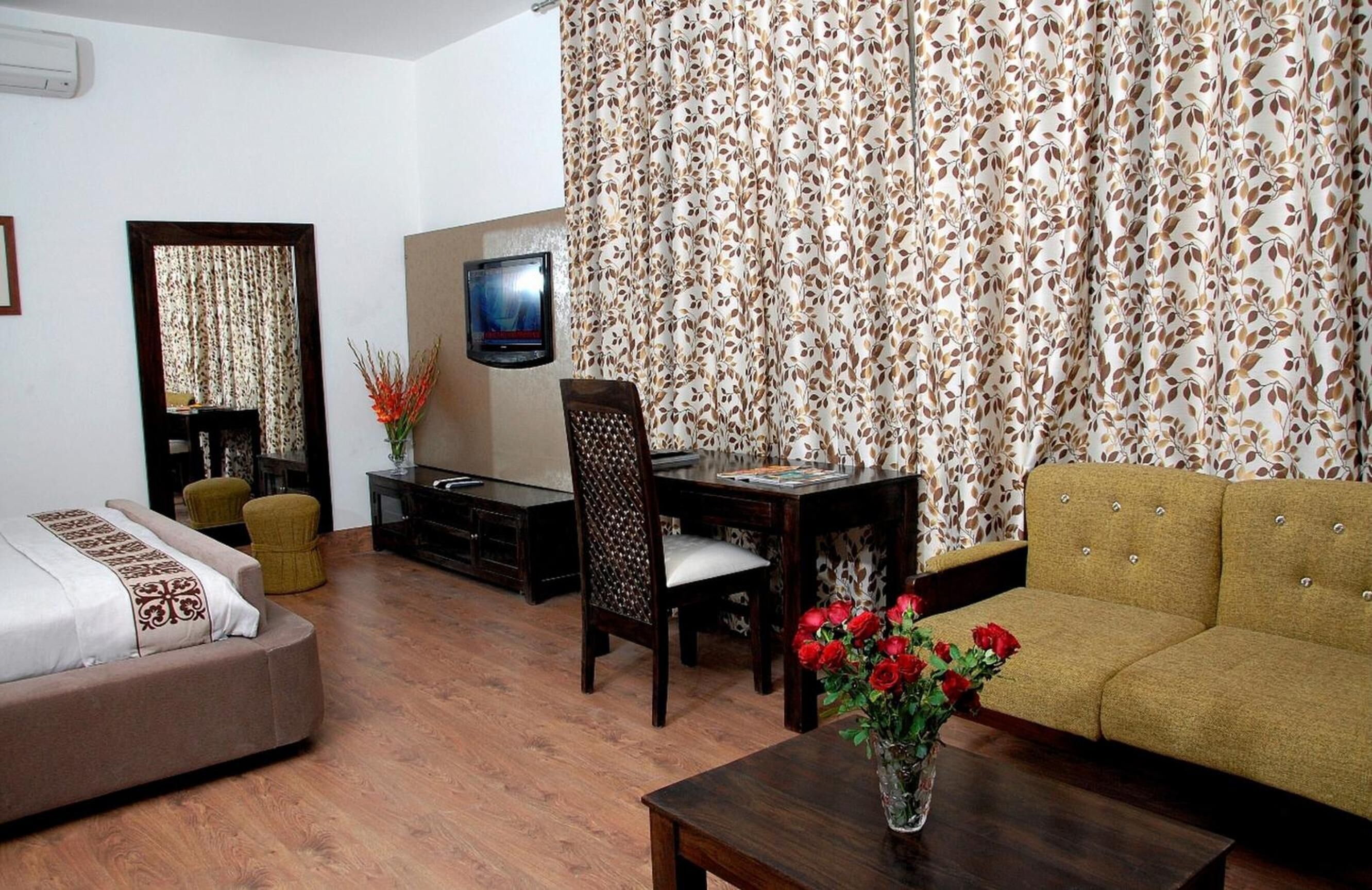 A room with a sofa, a dining table with chairs, a TV, and a mirror.