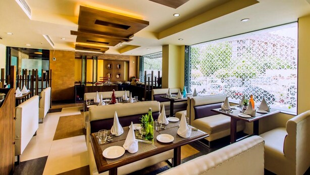 A modern restaurant with high tables and booths, a bar area, and large windows with a view. - 66 Residency - A Boutique Hotel (Jaipur)