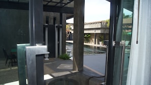 An outdoor patio area with a glass table and chairs, a small pool, and a view of a building with a tiled roof. - Green View Village Resort (Krabi)