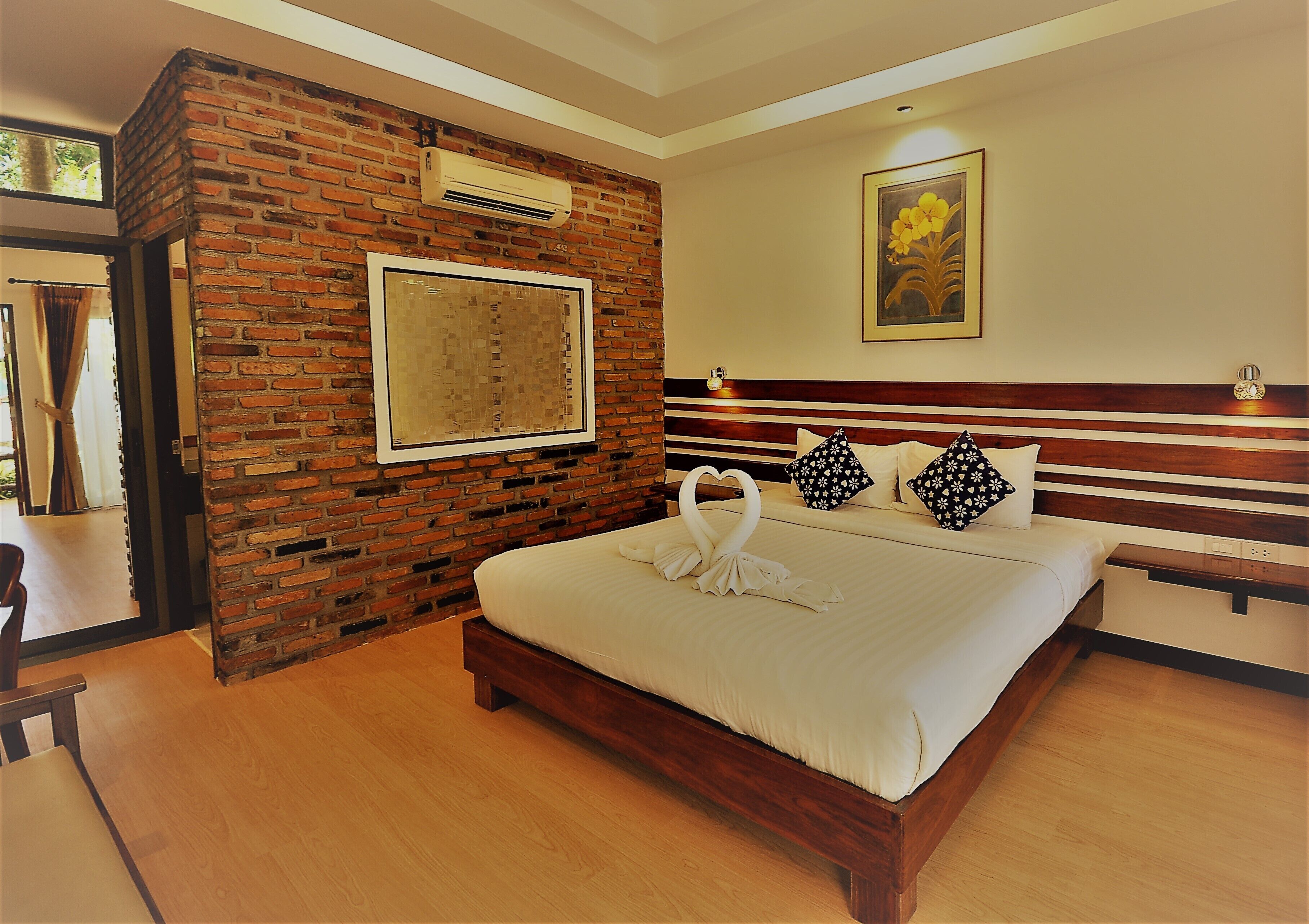 Habitación de hotel con pared de ladrillo, cama grande con ropa de cama blanca, cabecero de madera y un cuadro en la pared.