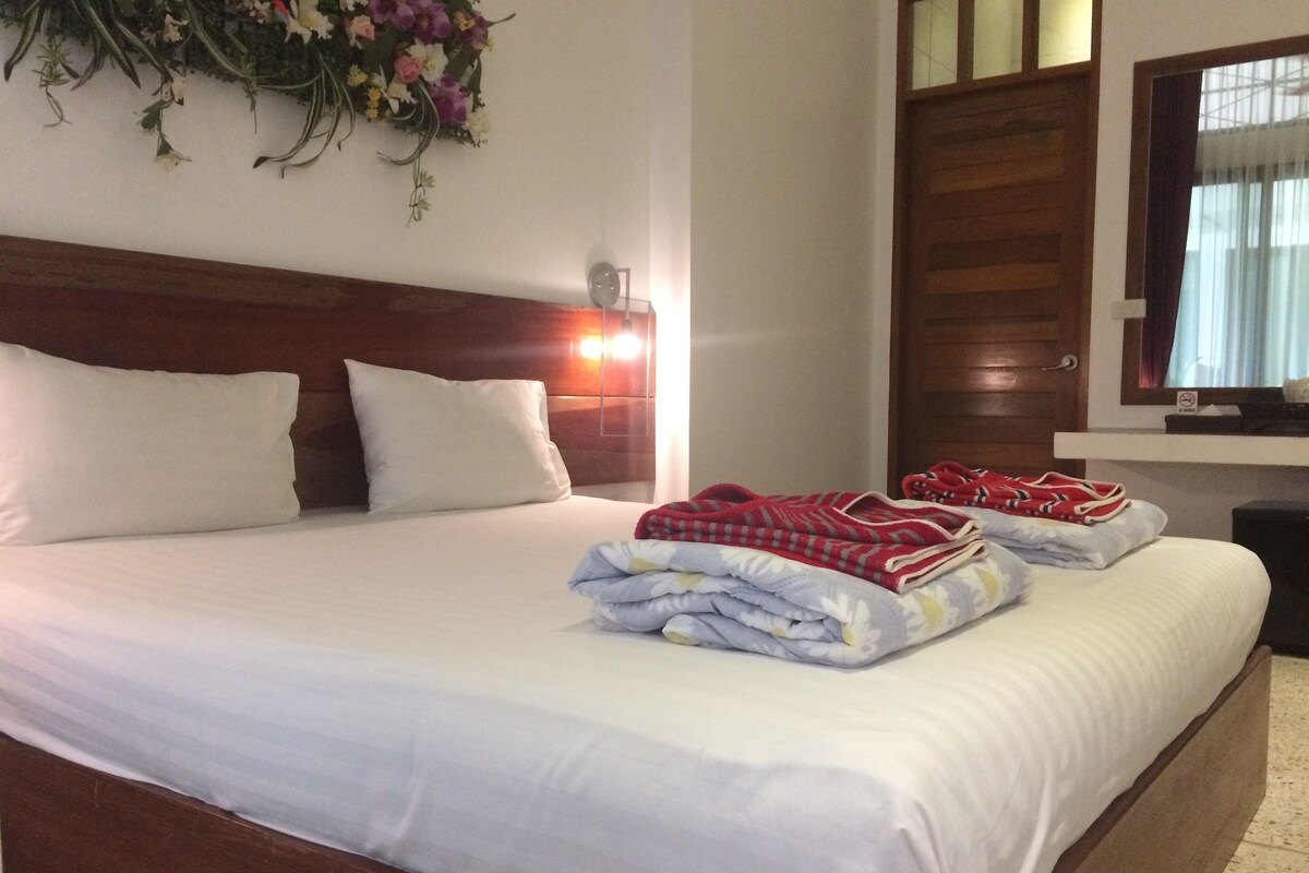 A neatly made bed with white linens, a wooden headboard, and a floral arrangement on the wall.