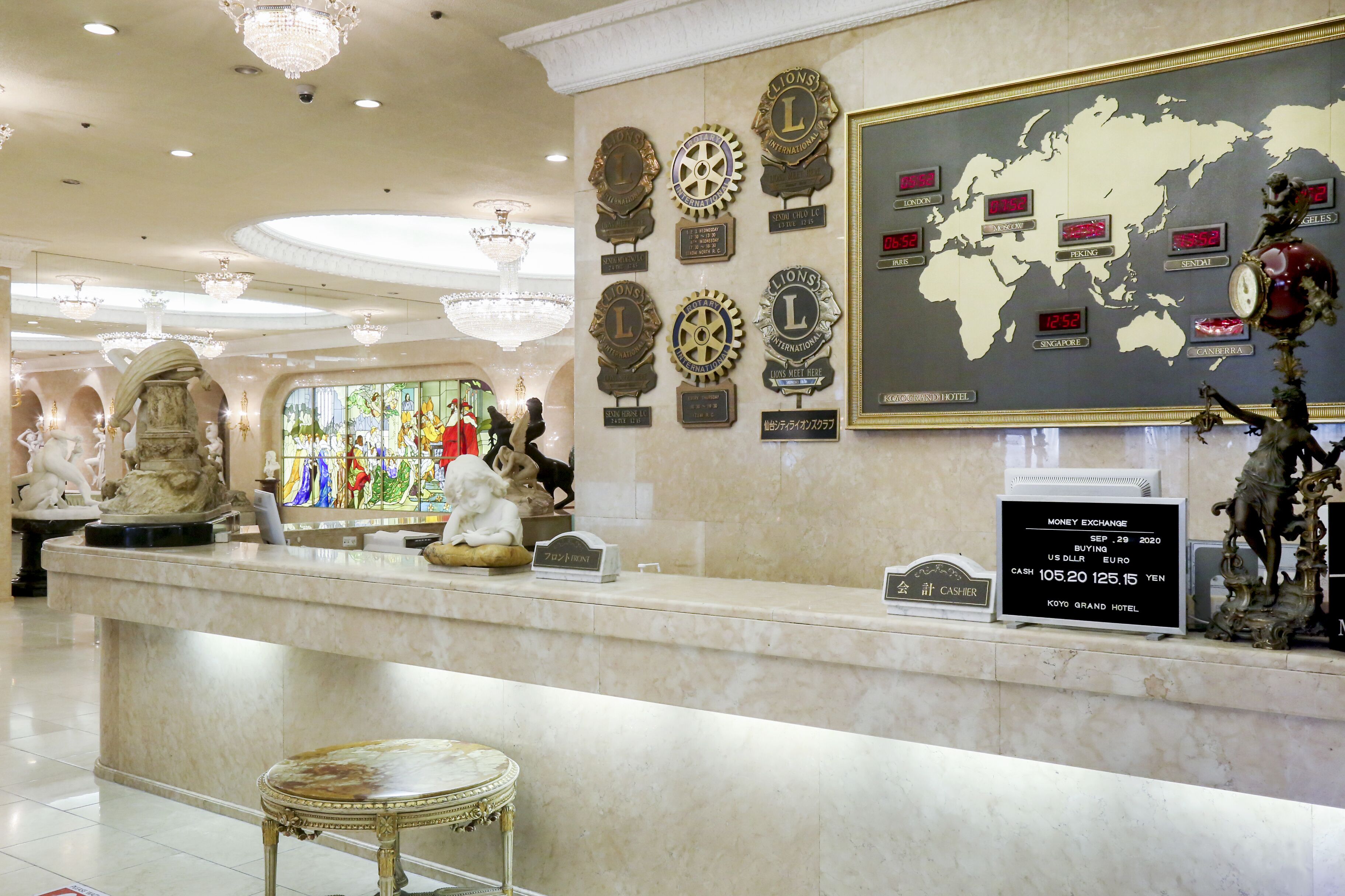 Een hotel receptie met een marmeren balie, een wereldkaart, klokken en informatie over valutawissel.
