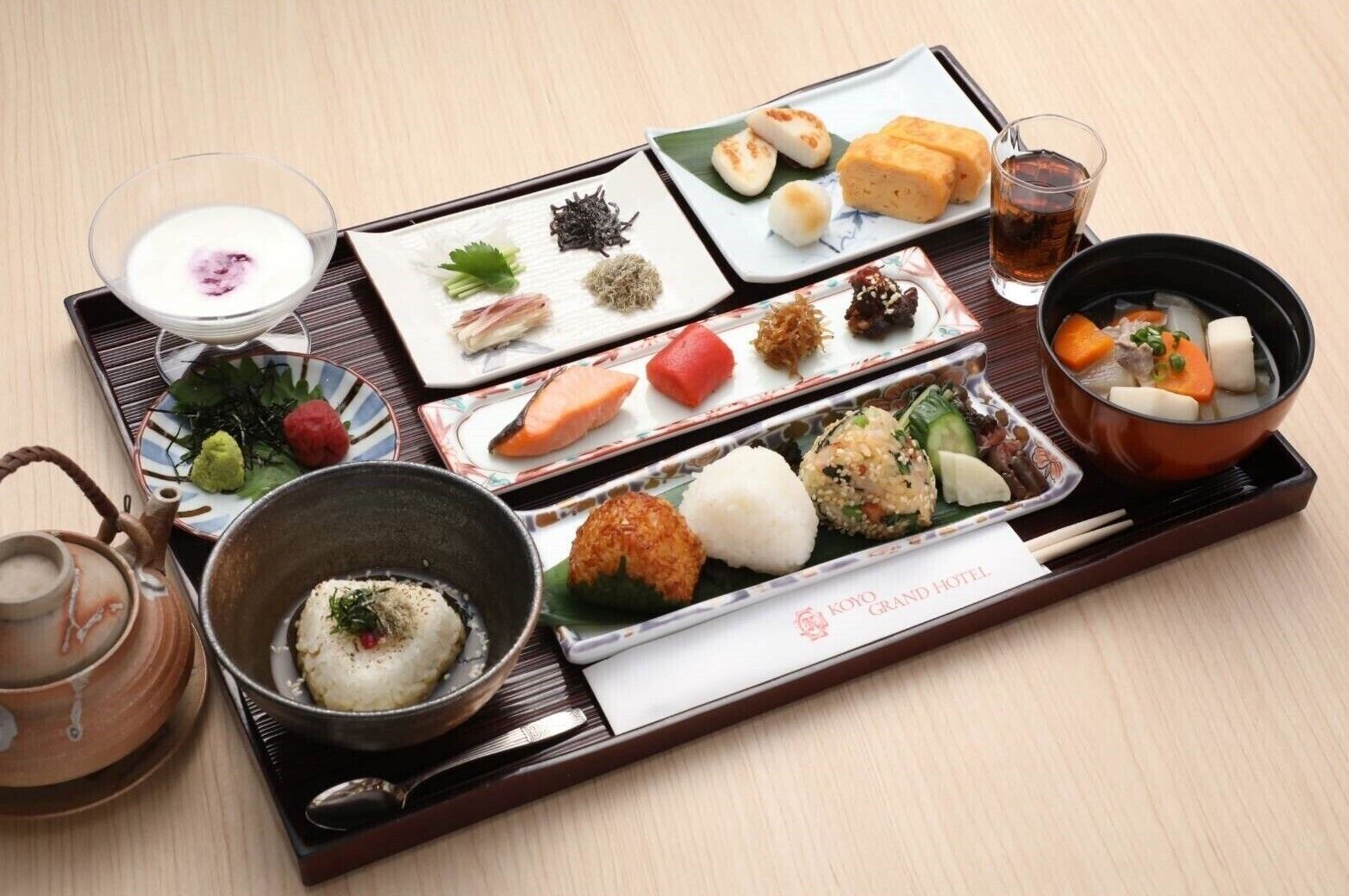 Un repas japonais traditionnel composé de différents plats et d’une théière, le tout présenté sur un plateau.