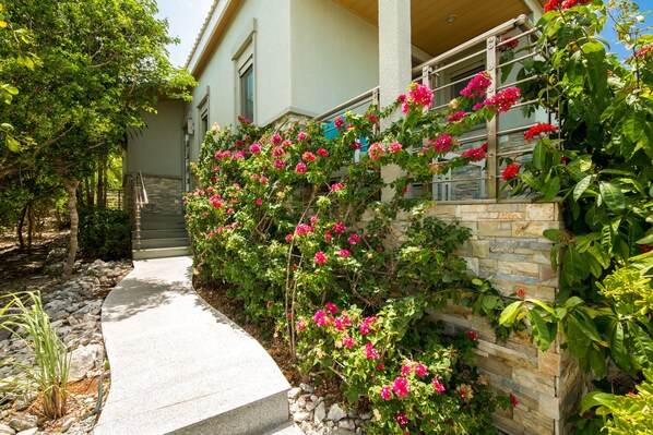 Un sendero que lleva a una casa con un muro de piedra y plantas con flores.