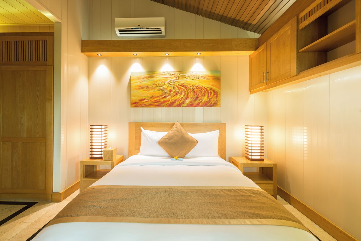 A hotel room with a large bed, wooden headboard, bedside lamps, and a painting on the wall.