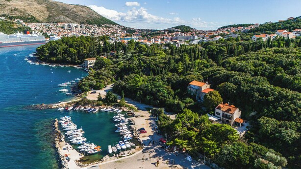 Un pueblo costero con un puerto deportivo, abundante vegetación y una mezcla de edificios residenciales y comerciales.