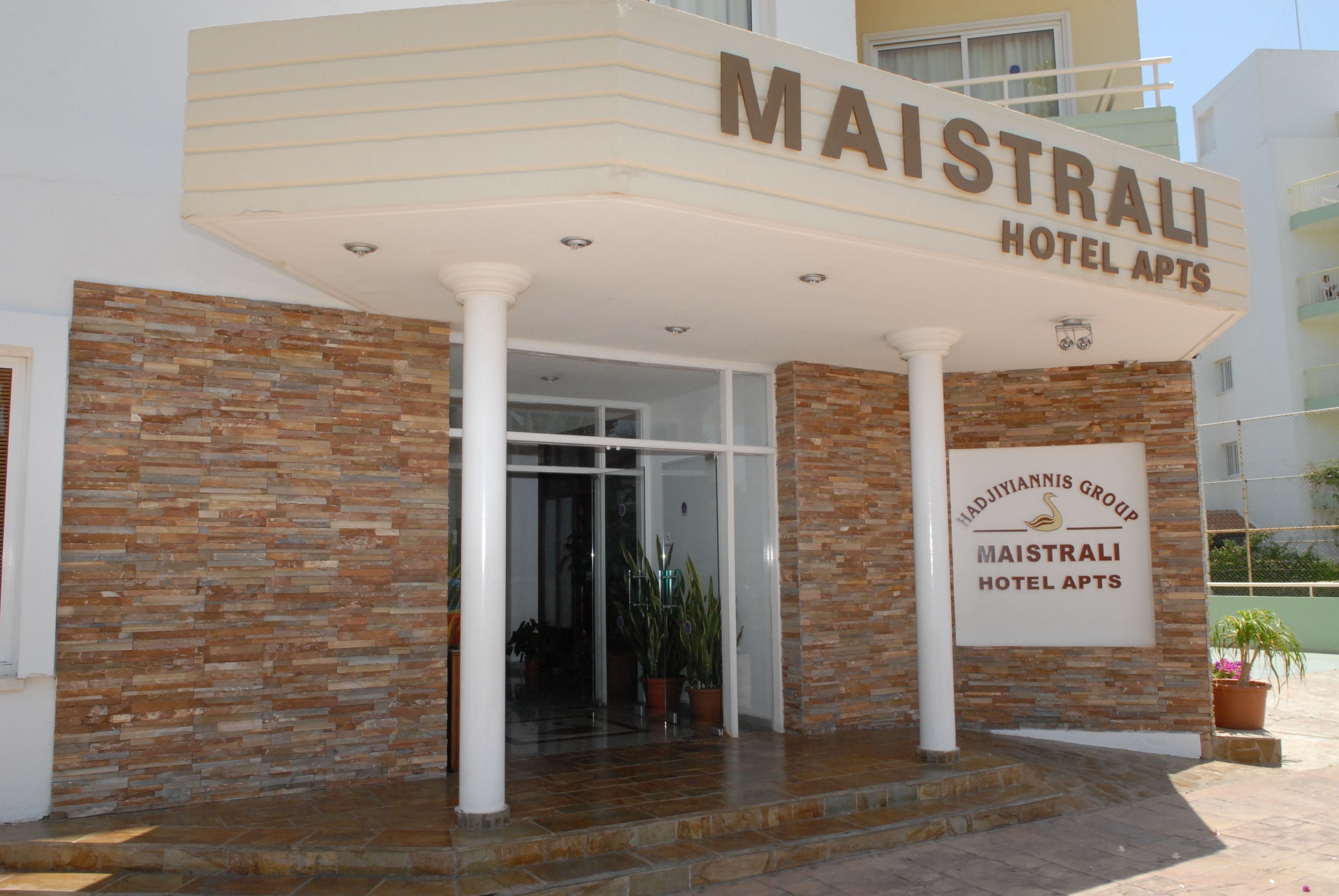 The exterior of Maistrali Hotel Apts, featuring a stone facade, a large signboard, and a well-lit entrance.