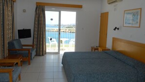 A hotel room with a bed, a TV, a balcony with a view of the sea, and a chair. - Maistrali Hotel Apts (Protaras)