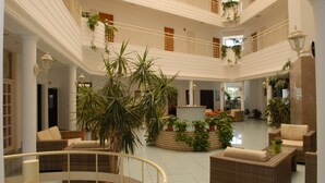 A spacious atrium with multiple levels, featuring wicker furniture, potted plants, and a central seating area. - Maistrali Hotel Apts (Protaras)