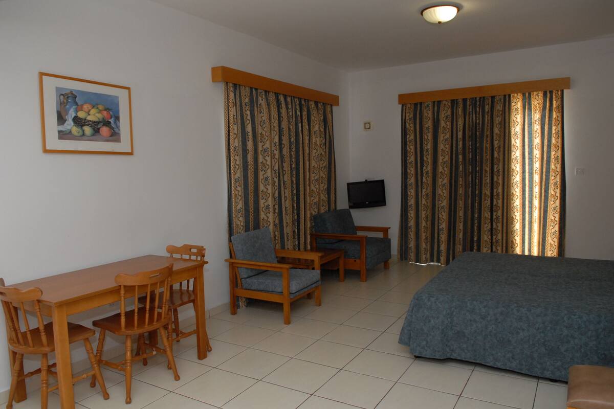 A room with a bed, a desk with chairs, a television, and curtains.