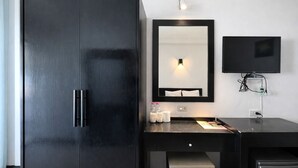 A hotel room with a large wardrobe, a desk with a mirror, a flat-screen TV, and a small refrigerator. - Phi Phi Chang Grand Resort & Spa (Ko Phi Phi)