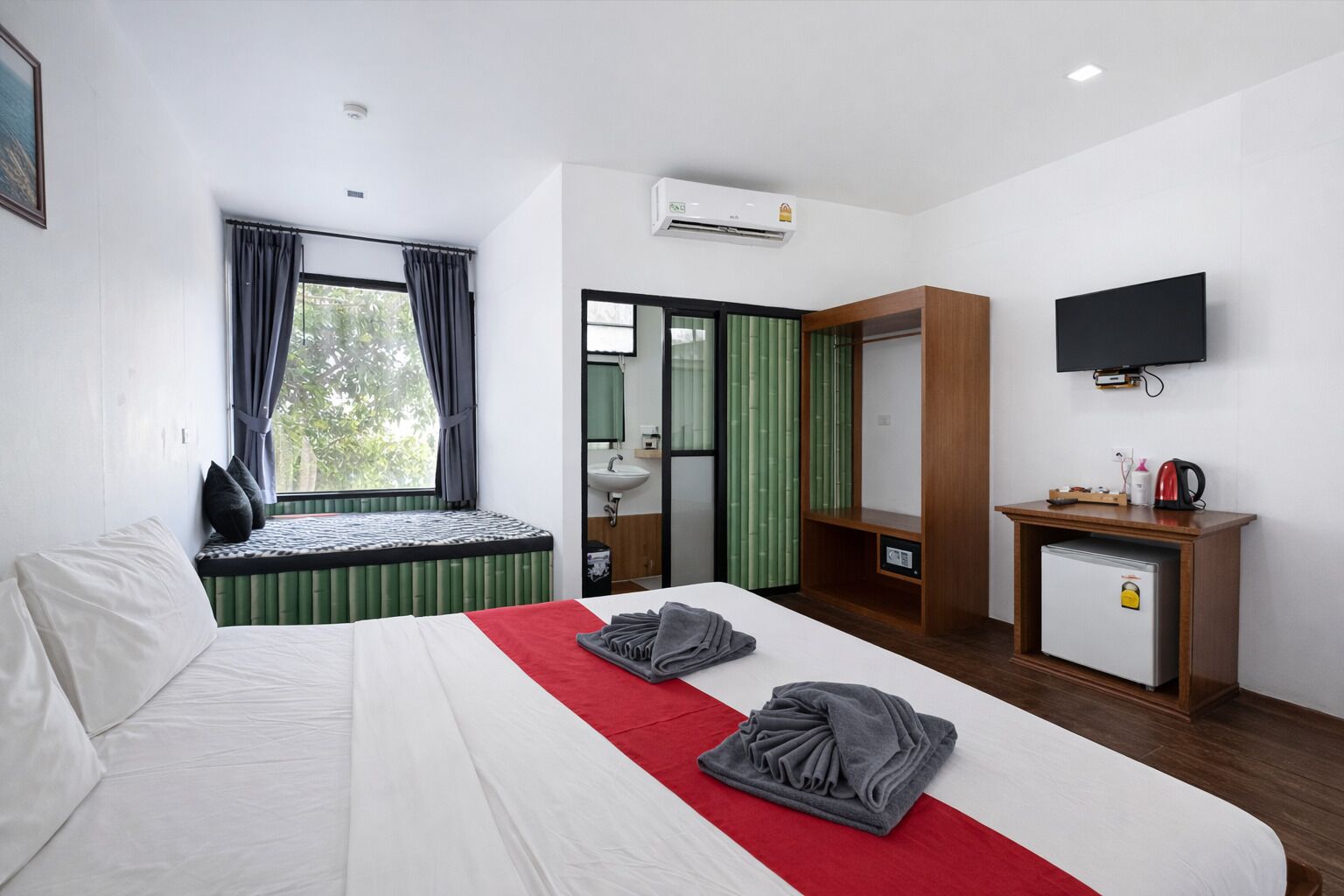 Una habitación de hotel con cama, escritorio, televisión y ventana con cortinas.