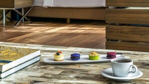 Une chambre d’hôtel avec un lit, des tables de chevet, une télévision et une table avec des pâtisseries et une tasse.